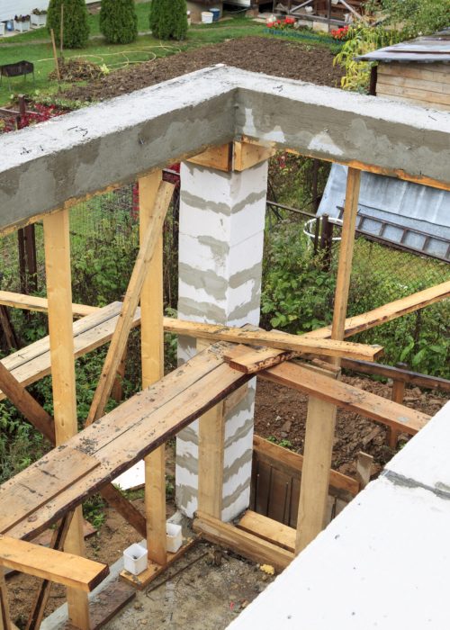Structure en cours de démolition avec poutres en bois, pilier en béton et débris, illustrant le processus de préparation pour un nouveau patio.