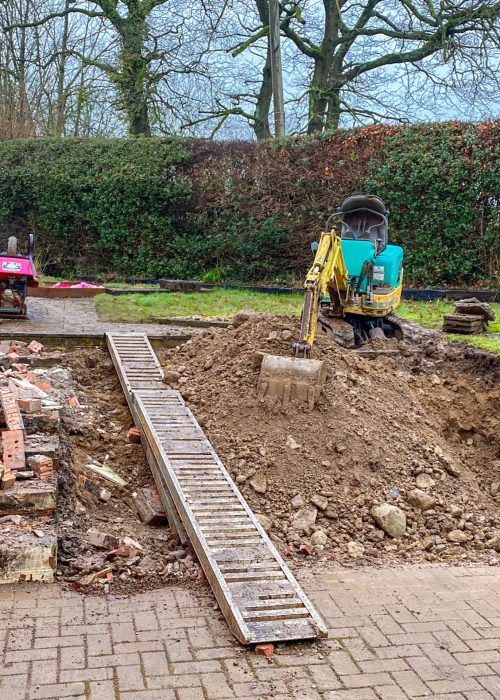 Excavatrice jaune sur un chantier résidentiel, avec un tas de terre et des matériaux de construction, illustrant les services d'excavation de Patio Exotic pour aménagement extérieur.