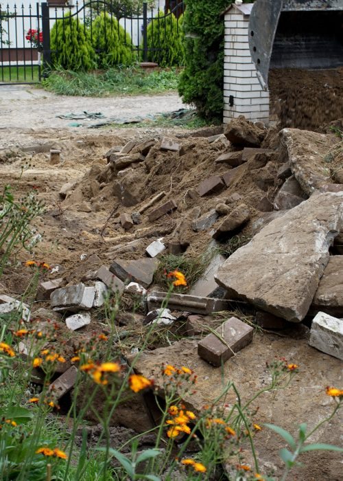 Chantier de fondation avec gravats, terre et fleurs, illustrant les préparatifs pour l'installation d'un patio par Patio Exotic.