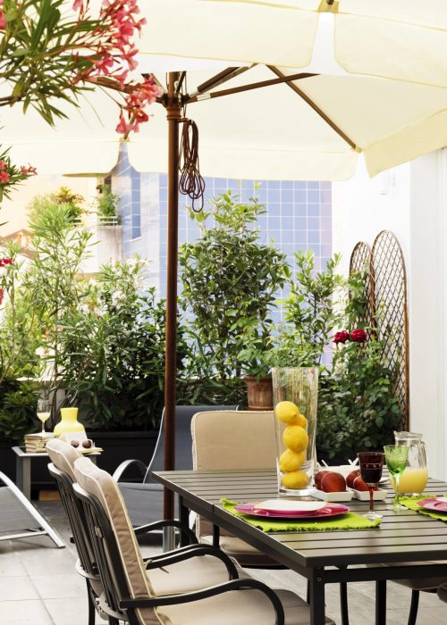 Espace patio clé en main avec table de repas, chaises confortables, parasol, et décor floral, illustrant l'aménagement extérieur proposé par Patio Exotic.