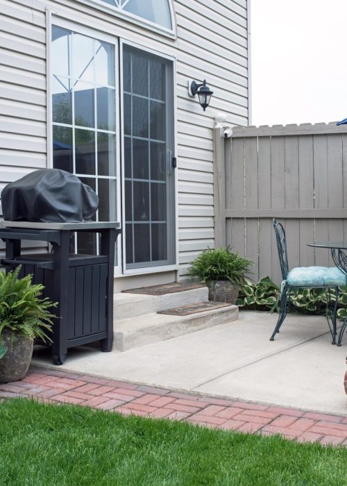 Espace extérieur avec patio, barbecue couvert, chaise en fer forgé, et clôture en bois, illustrant les services de conception et d'installation de patios et clôtures sur mesure de Patio Exotic.
