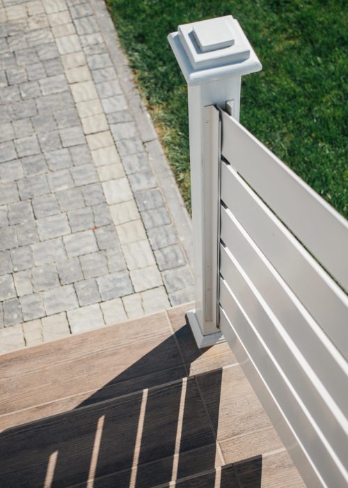 Rampe de patio moderne en bois avec balustrade blanche, vue sur le sol en pavés et gazon, illustrant l'esthétique et la sécurité des installations de Patio Exotic.