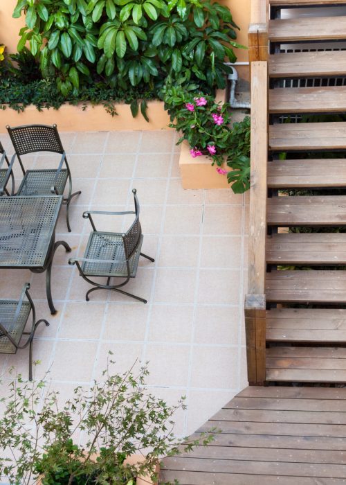 Espace extérieur avec table et chaises en métal, plantes vertes et escalier en bois, illustrant une installation de patio sur mesure.