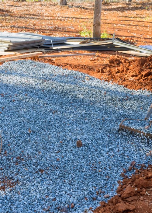 Préparation de fondation en gravier pour patio, sol stabilisé, matériaux de construction en arrière-plan, projet d'aménagement extérieur.
