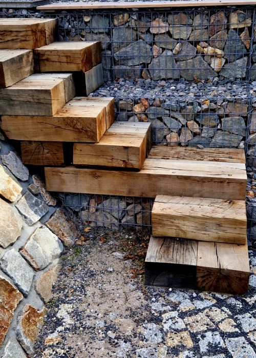 Escalier en bois avec des marches en bois massif, entouré de pierres et de gravier, illustrant un aménagement extérieur de patio sur mesure.