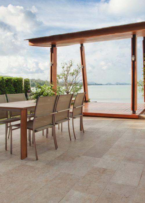 Terrasse moderne avec table en bois et chaises, vue sur l'eau, entourée de verdure, représentant l'expertise de Patio Exotic en aménagement extérieur.