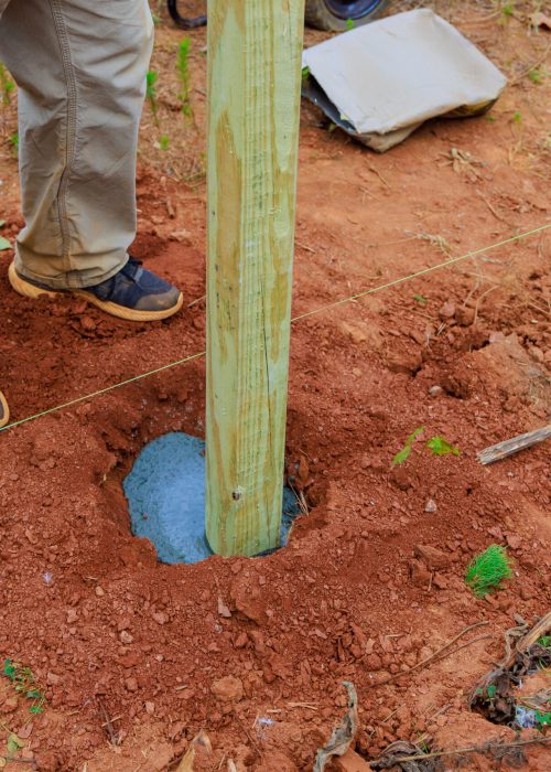 Pieu en bois installé dans un trou de fondation, avec béton frais visible, illustrant le processus de construction de patio par Patio Exotic.