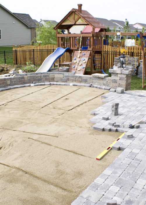 Terrasse en construction avec sable et pavés, espace extérieur adapté pour une aire de jeux, intégration de matériaux durables et esthétiques.
