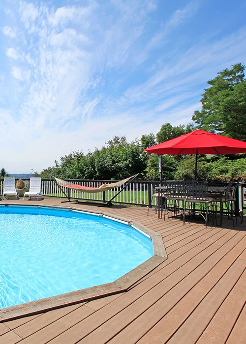 Terrasse en bois autour d'une piscine, avec chaises longues, hamac, et parasol rouge, illustrant un espace extérieur accueillant pour la détente et la sécurité.