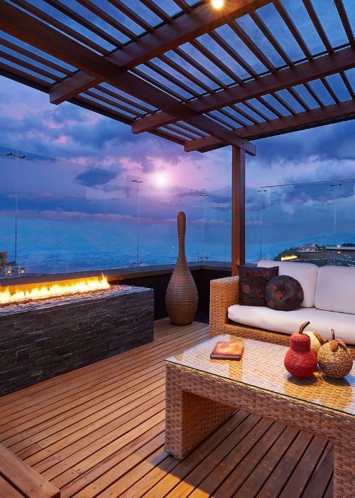 Conception de patio avec pergola – Patio Exotic Patio moderne avec canapé blanc, table en osier, cheminée au gaz, décor élégant, sous une pergola en bois, vue panoramique au crépuscule.